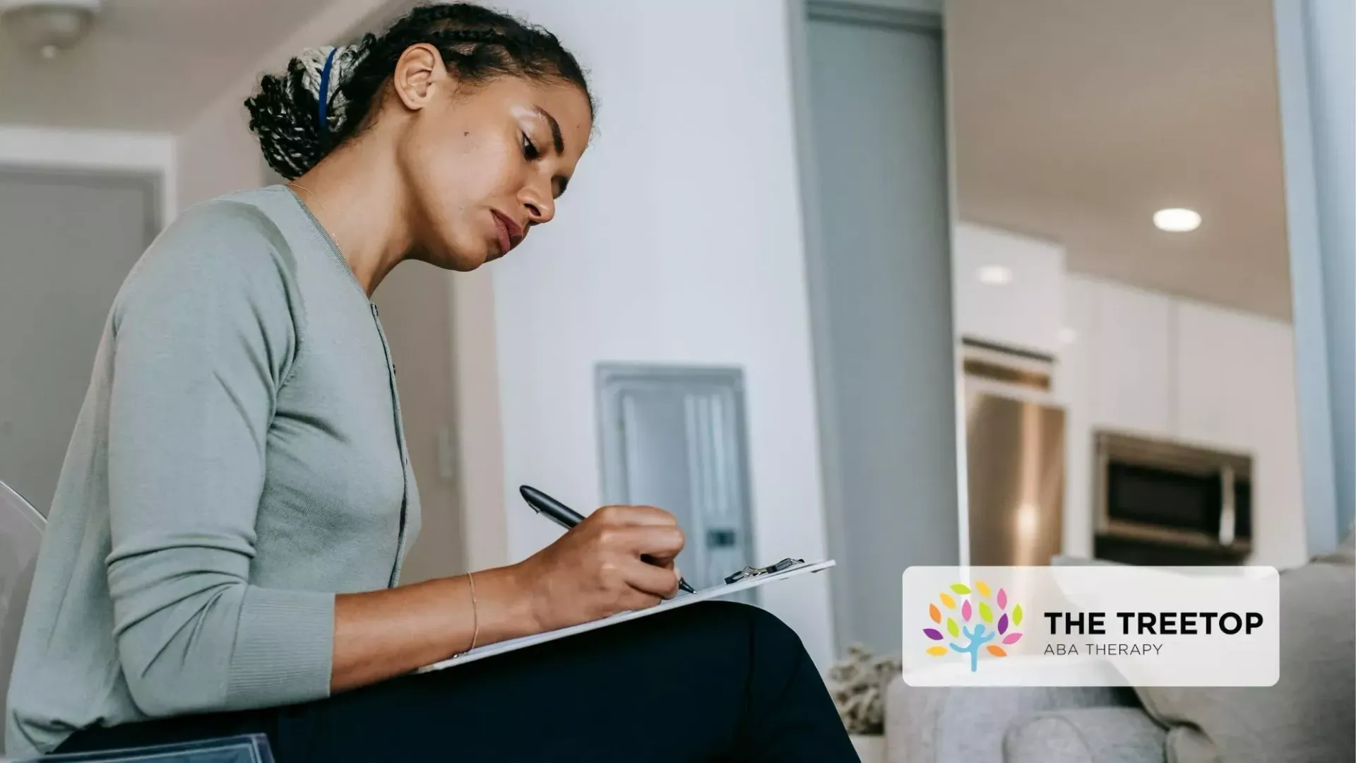 Person writing in a notebook on a couch in a modern living room, focused on work