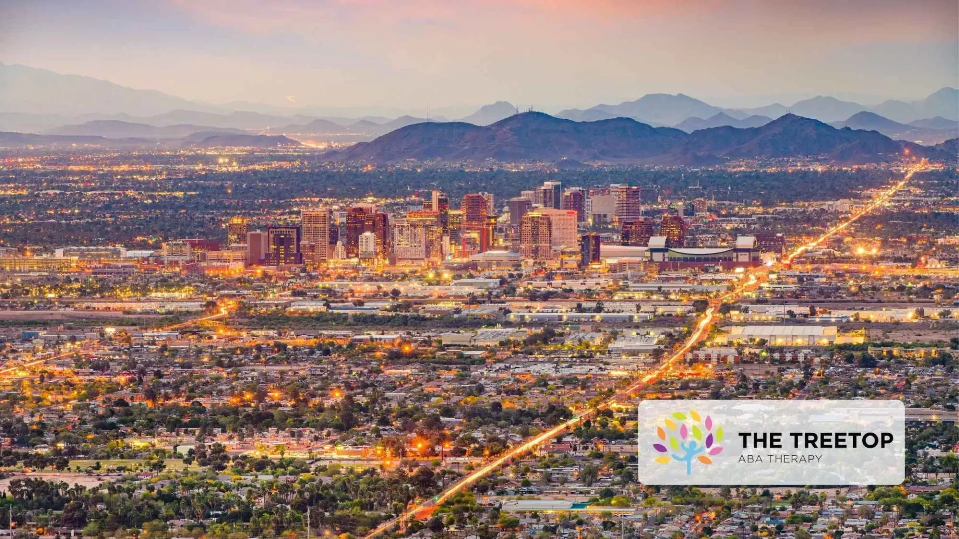 Aerial view of a city skyline at dusk with glowing streets and mountains in the distance.