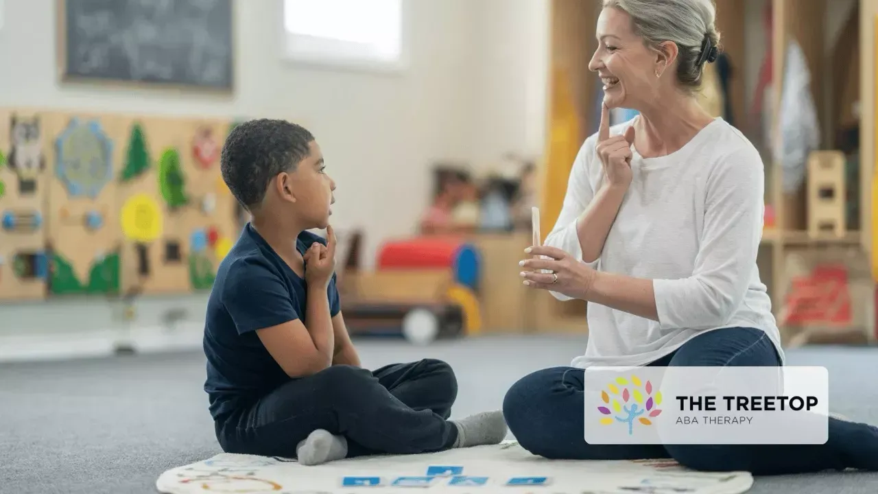 Teacher and child sitting on a classroom floor, talking and playing with blocks at The Treetop preschool.