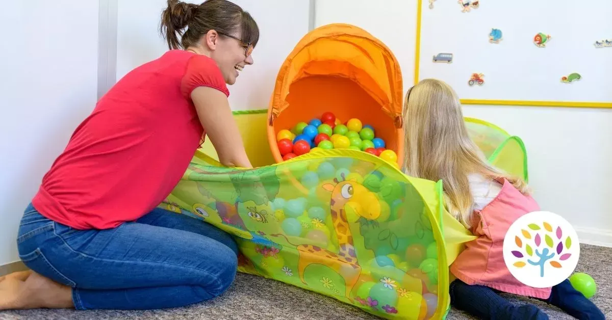 An adult and child play together in a colorful, giraffe-themed pop-up ball pit in a brightly lit room.
