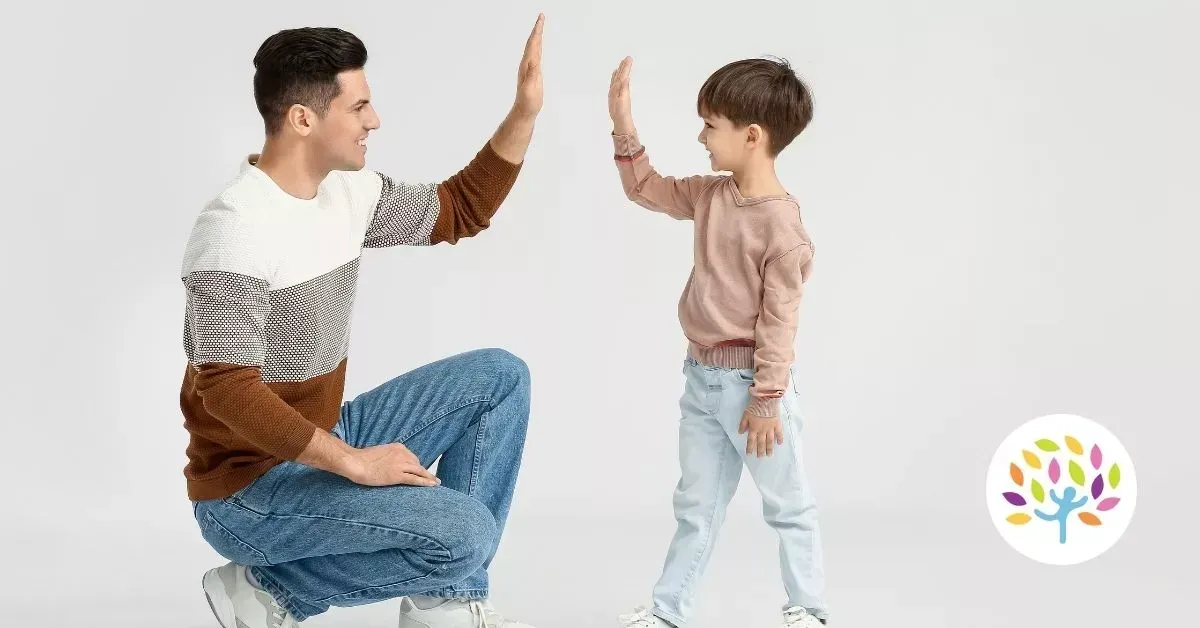 Man and child facing each other, giving a high five in a bright studio setting.