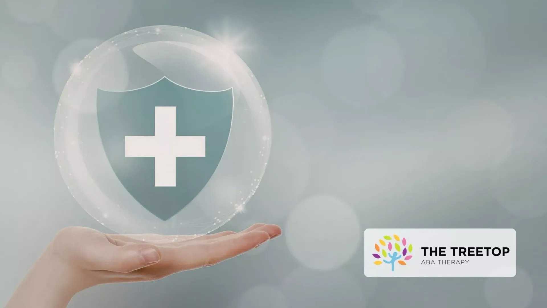Hand holding a glowing shield with a white medical cross on a soft gray background