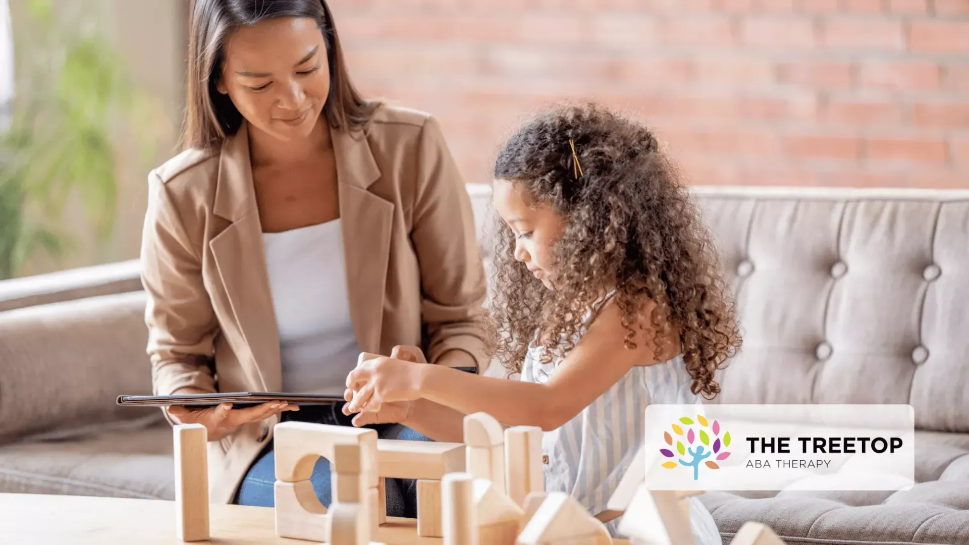 A therapist observes a child playing with wooden blocks on a table in a bright, modern living room.