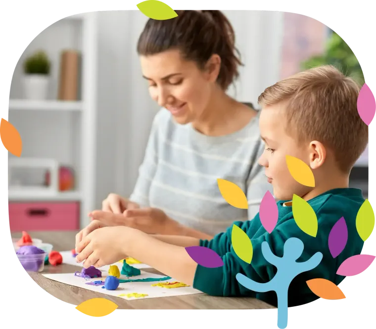 A person and a child sit at a table, smiling while playing with colorful modeling clay on paper in a bright room.
