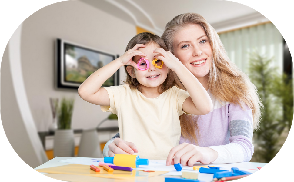 A person and a child smile while crafting at a table; the child holds colorful shapes over their eyes like glasses.