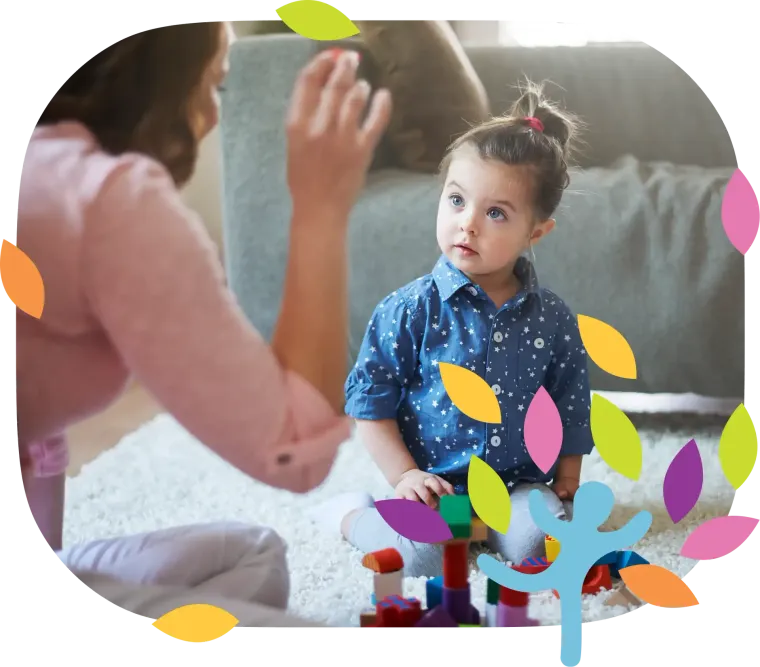 A person interacts with a child playing with colorful building blocks on a rug in a bright, indoor setting.
