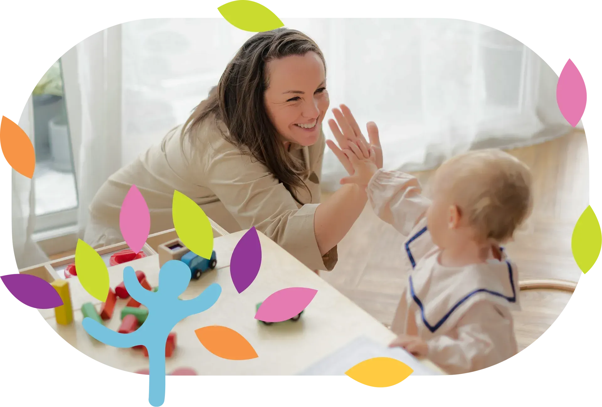 A person giving a high-five to a toddler in a brightly lit room with a table of toys and decorative colorful leaves.