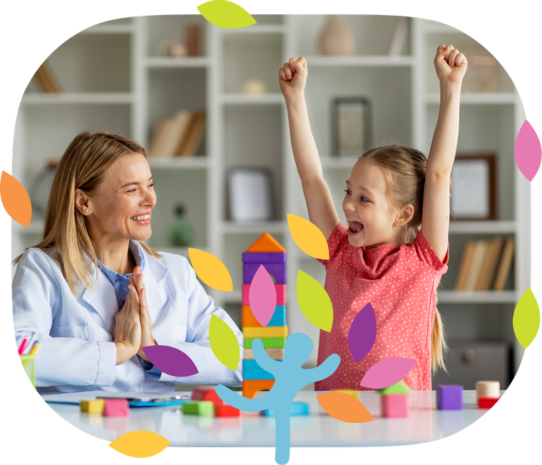 A therapist sits with a child who is cheering with arms raised next to a colorful toy block tower in a bright office.