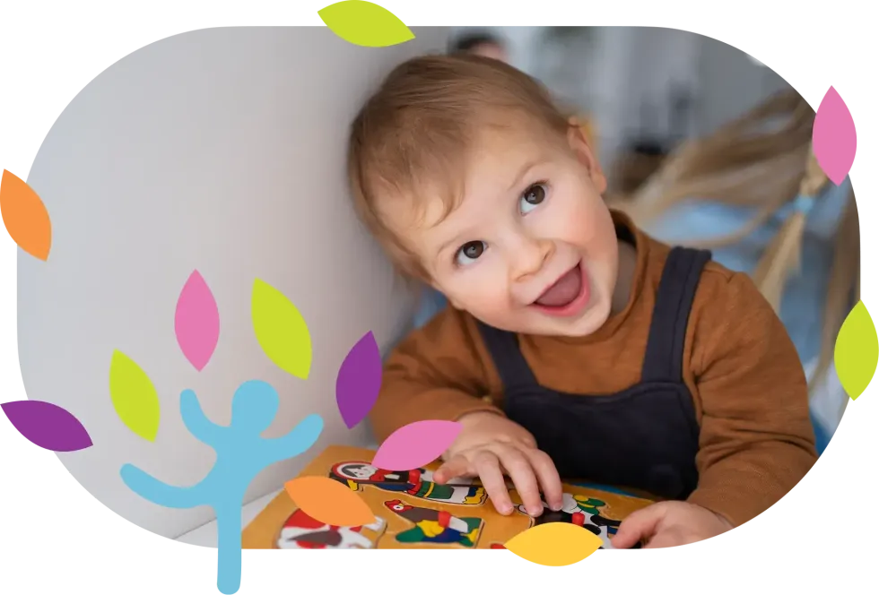 A smiling child leans against a wall while playing with a colorful wooden puzzle, framed by stylized decorative leaves.