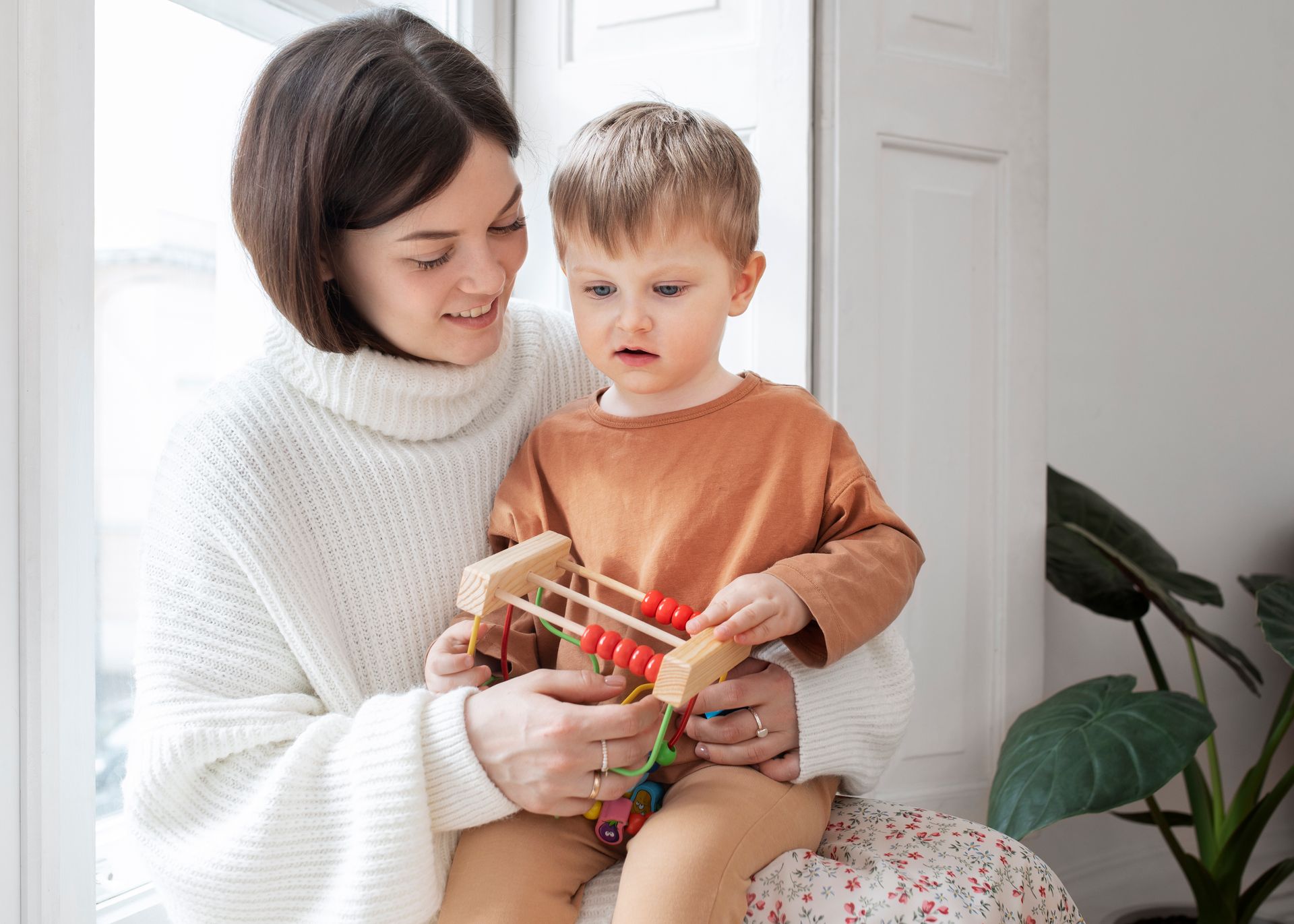 Young boy sitting on his mom's lap and playing with a toy