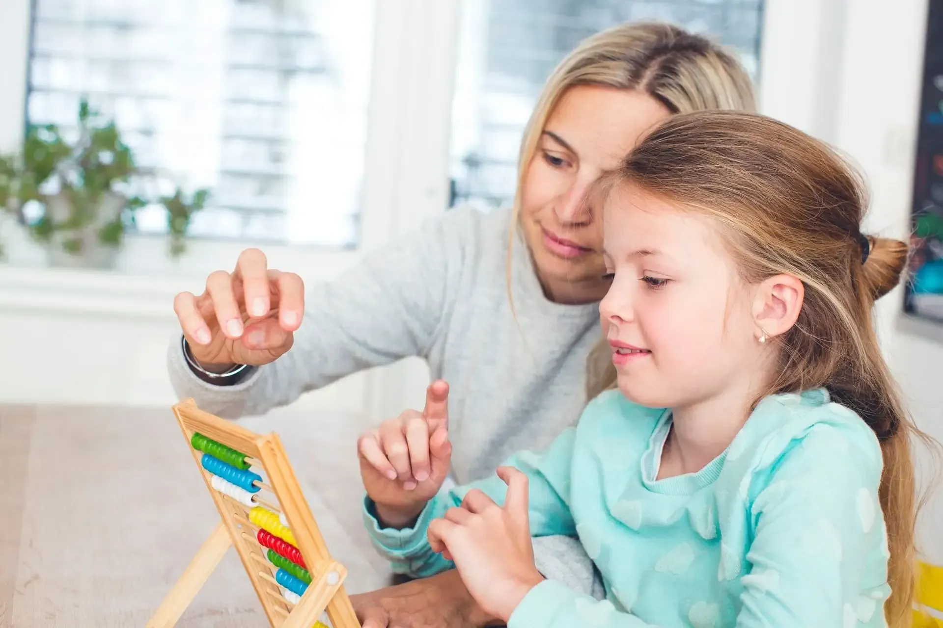 A person helping a young child use a small wooden abacus with colorful beads while sitting at a table.