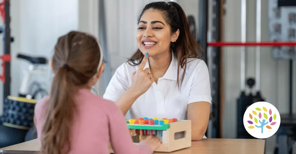 A professional instructor gestures toward her mouth while working with a student on speech therapy exercises.