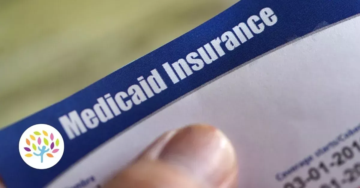 A close-up view of a hand holding a blue Medicaid Insurance card.