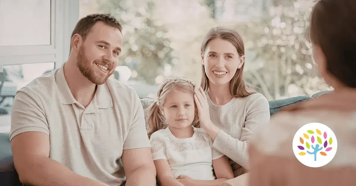 A family sits together smiling while talking to a professional in a bright, indoor setting.