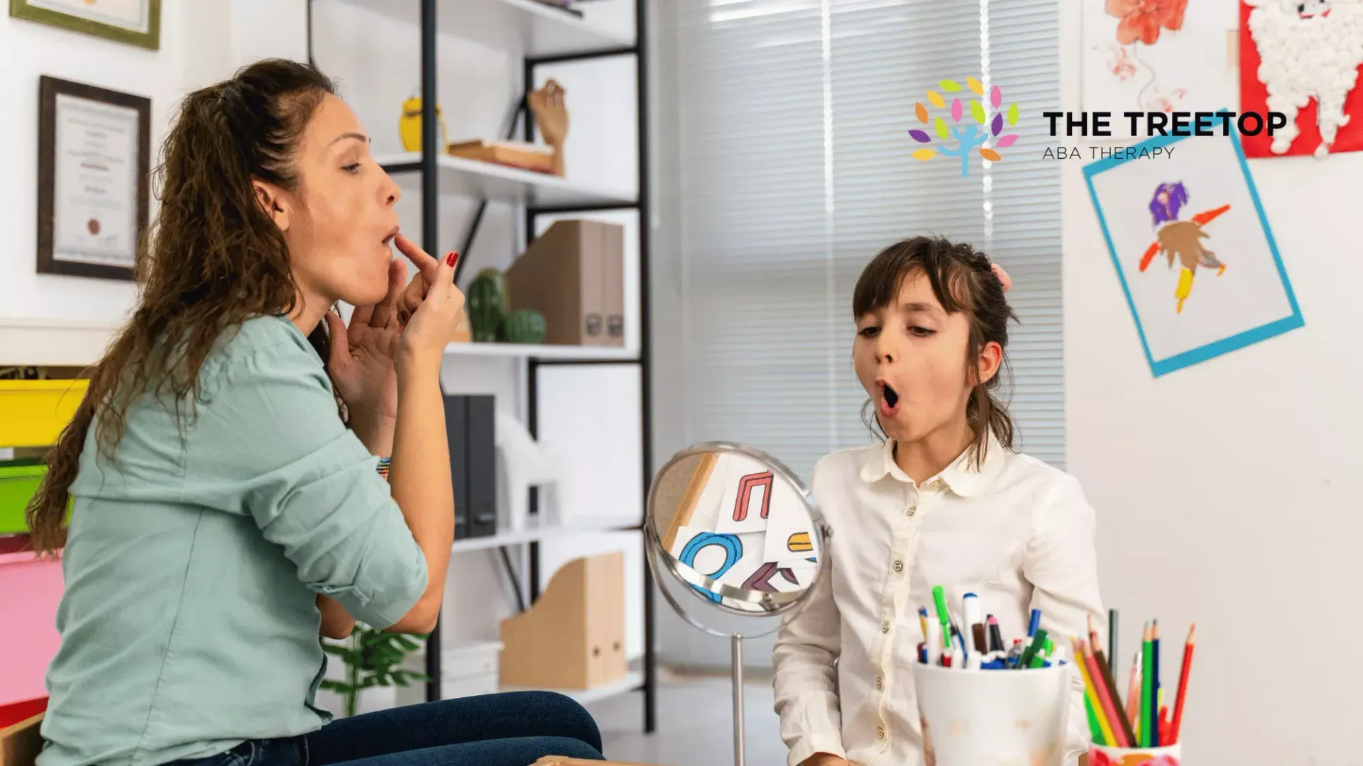 ABA therapist  demonstrates mouth movements to a child, using a mirror for speech therapy in a room.