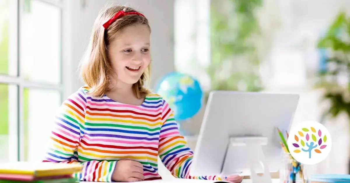 A person in a rainbow-striped shirt smiling while using a computer at a desk with a globe in the background.