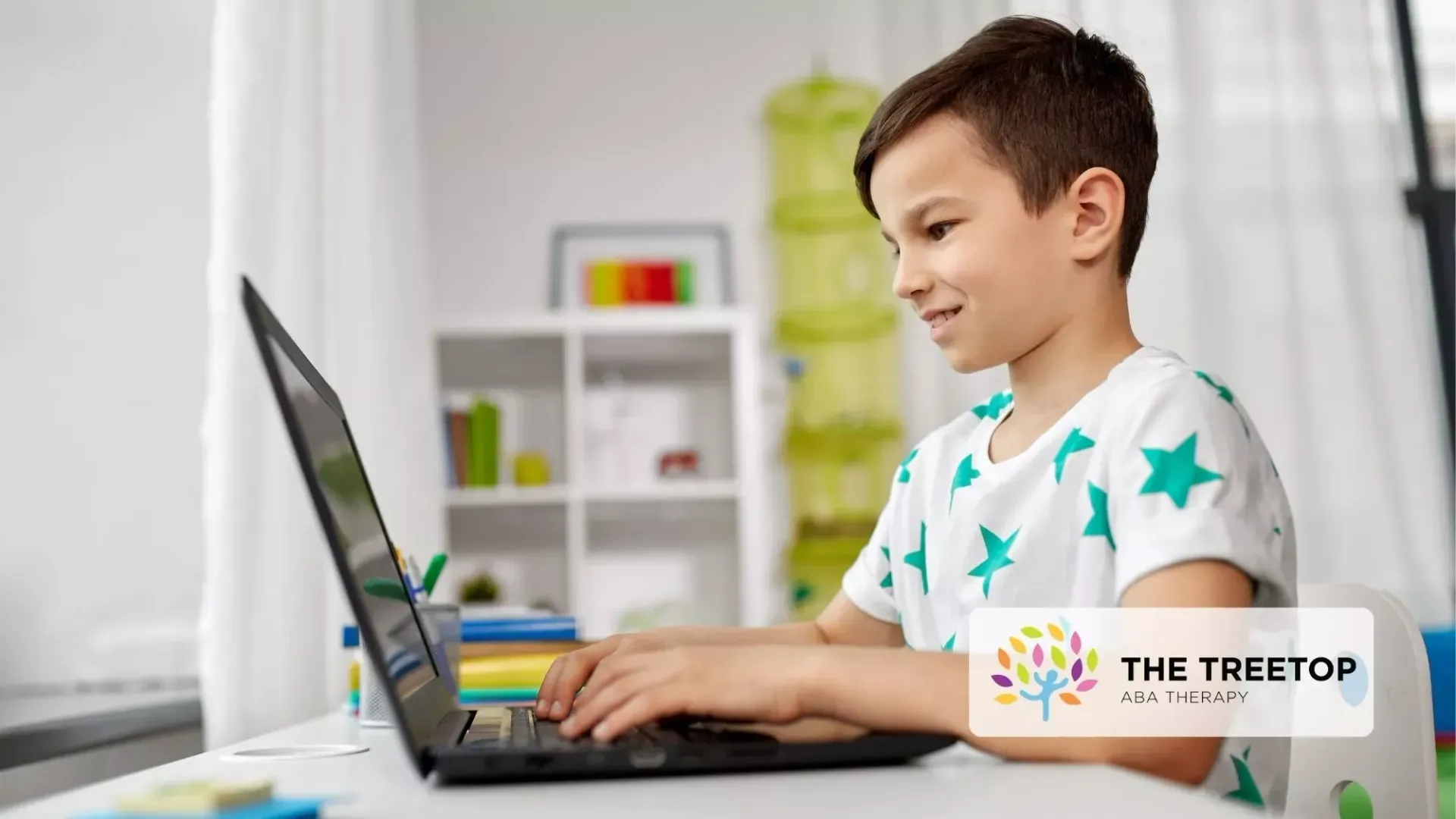 A person with a cheerful expression typing on a laptop at a table in a brightly lit room.