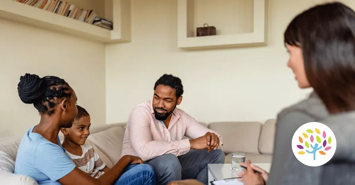 A family sitting on a couch in a bright room, speaking with a professional during a counseling or consultation session.