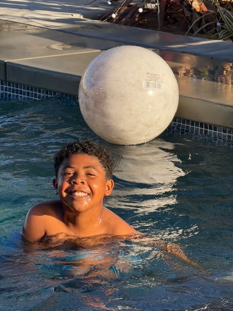 A smiling child swimming in a pool next to a large, light-colored inflatable ball.