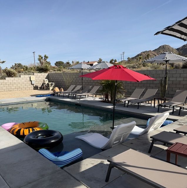 A swimming pool in a desert setting with mountains in the background, featuring floating rings and lounge chairs.