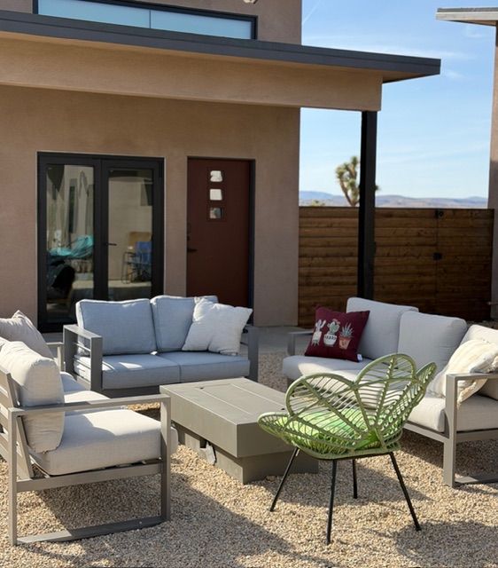 Outdoor seating area with gray sofas, a central coffee table, and a green accent chair on a gravel patio by a house.