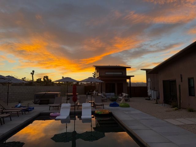 A vibrant sunset over a swimming pool with lounge chairs and desert landscaping in the background.