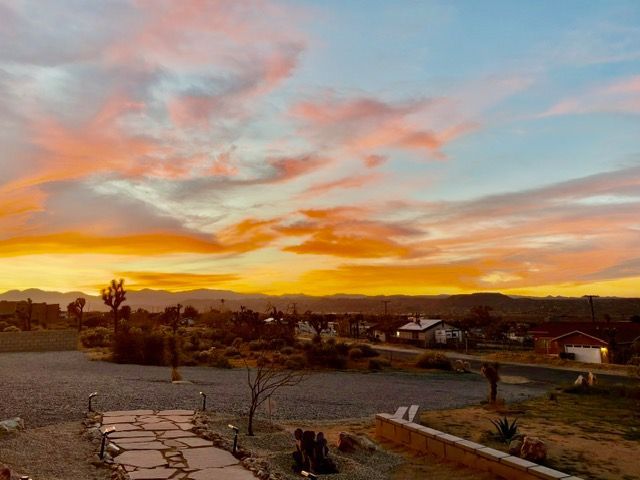 A vibrant sunset with pink and orange clouds over a desert landscape with scattered houses and a stone path.