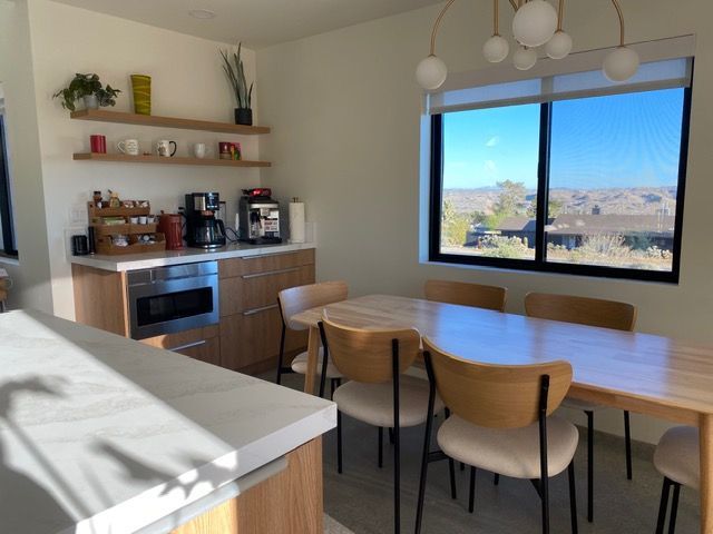 A bright modern kitchen with a wooden dining table and chairs near a window looking out onto a landscape.