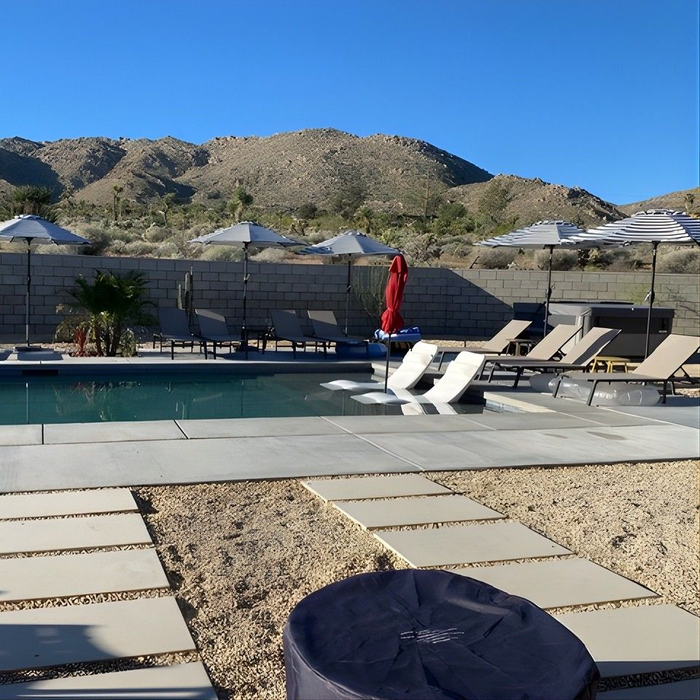 Pool with lounge chairs, desert landscape with mountains in background.