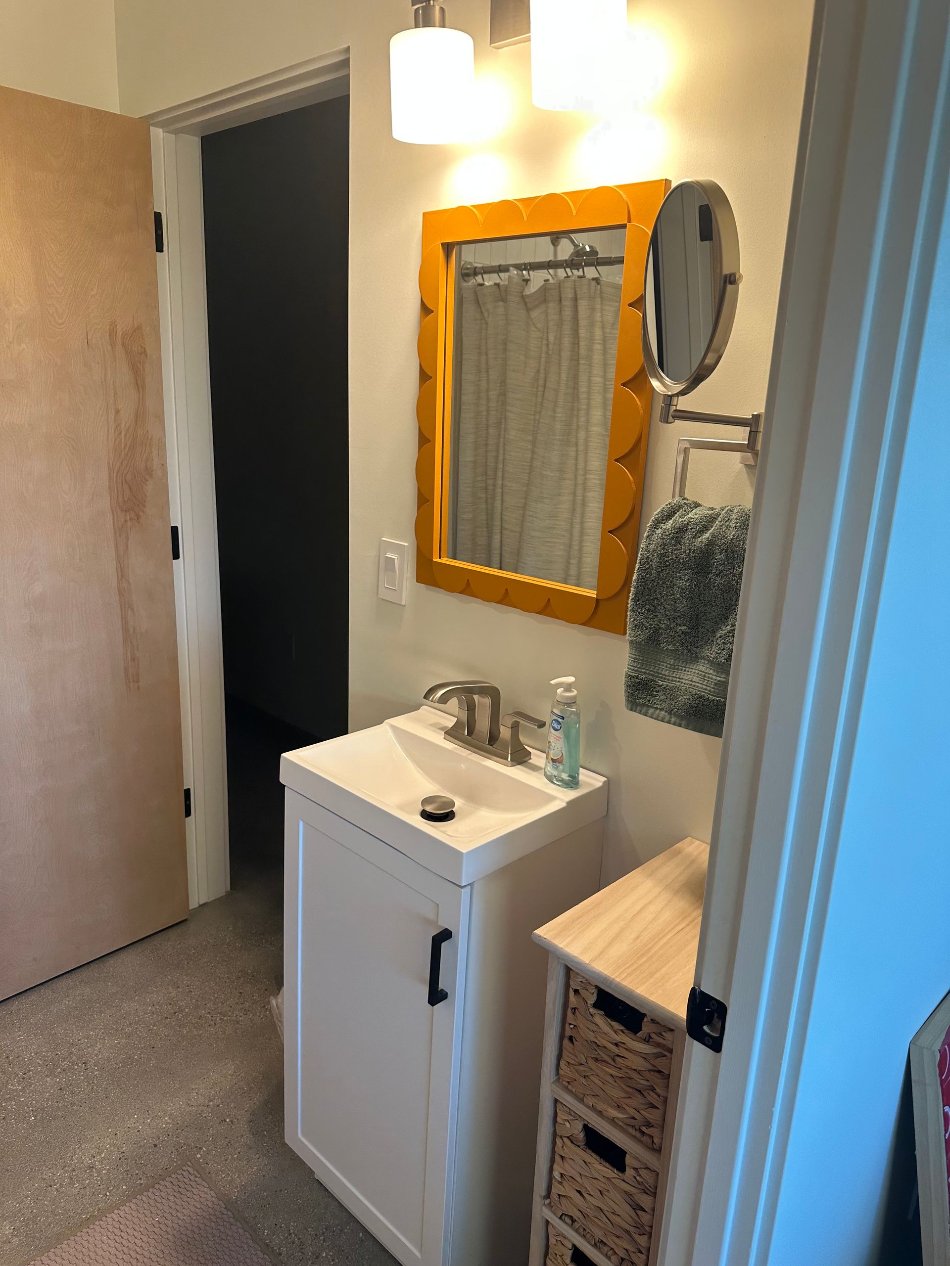 Bathroom with white vanity, mirror with yellow frame, and open doorway.