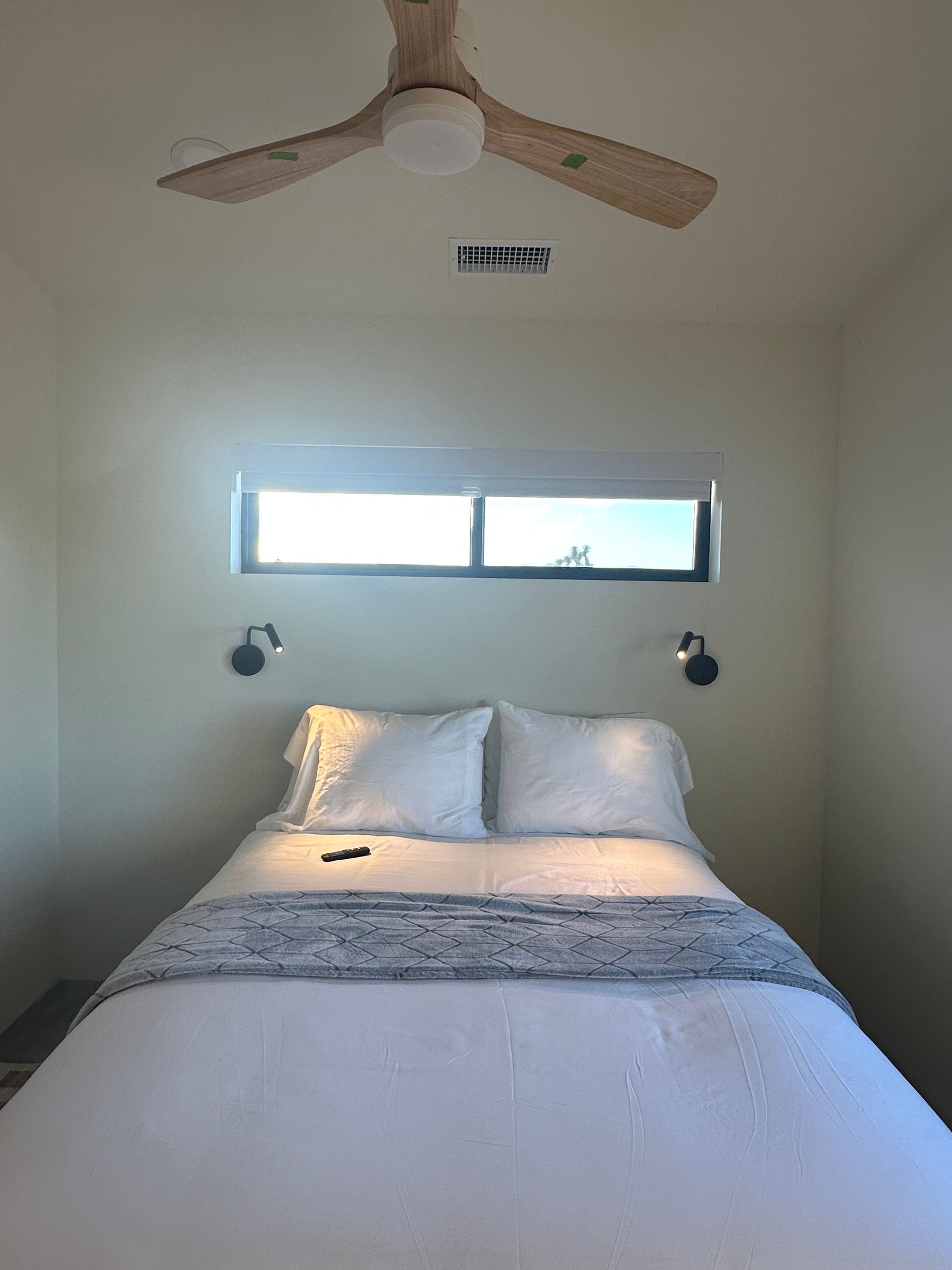 Bedroom with bed, small window, ceiling fan, and sconce lights.