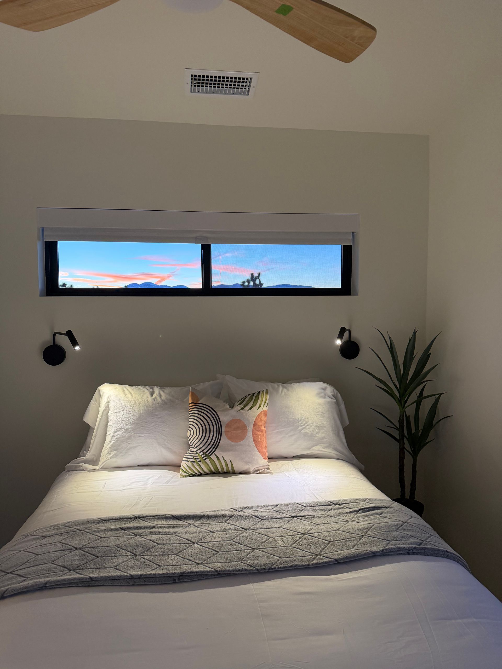 Bedroom with bed, pillows, window with view, sconces, and a ceiling fan.