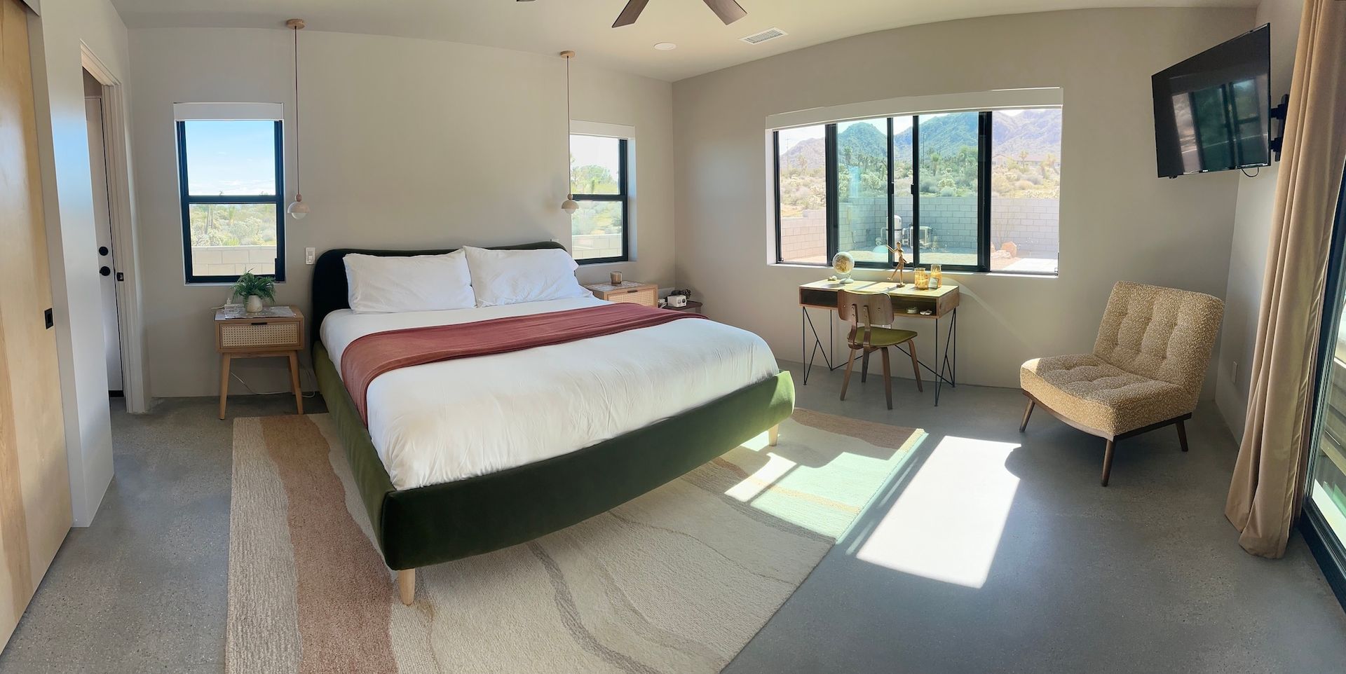 Bedroom with a bed, desk, and chair. Large windows provide natural light.