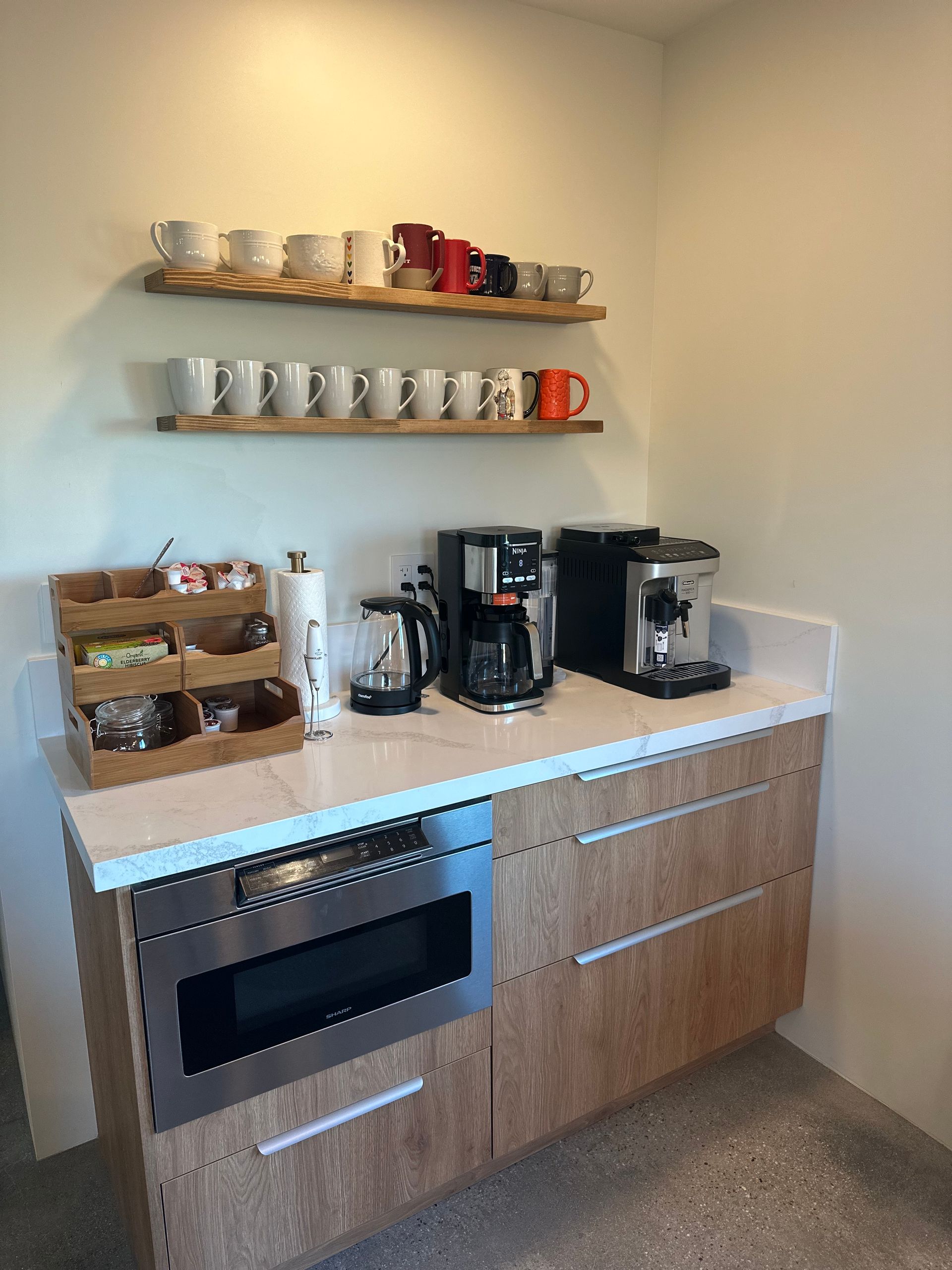Coffee station with coffee makers, mugs on shelves, microwave, and tea.