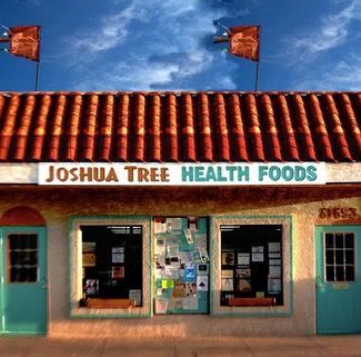 Joshua Tree Health Foods store front with a red tile roof, turquoise doors, and a bulletin board between two windows.