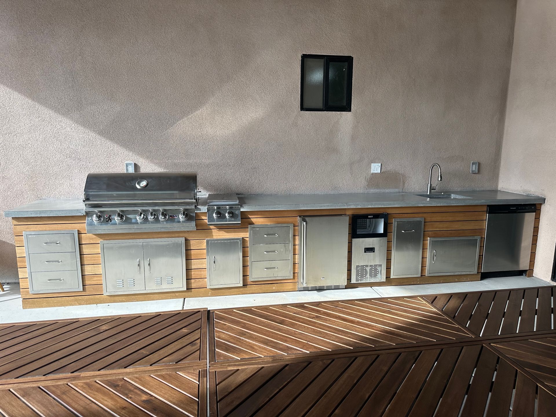 Outdoor kitchen with stainless steel appliances and wood paneling on a wooden deck.