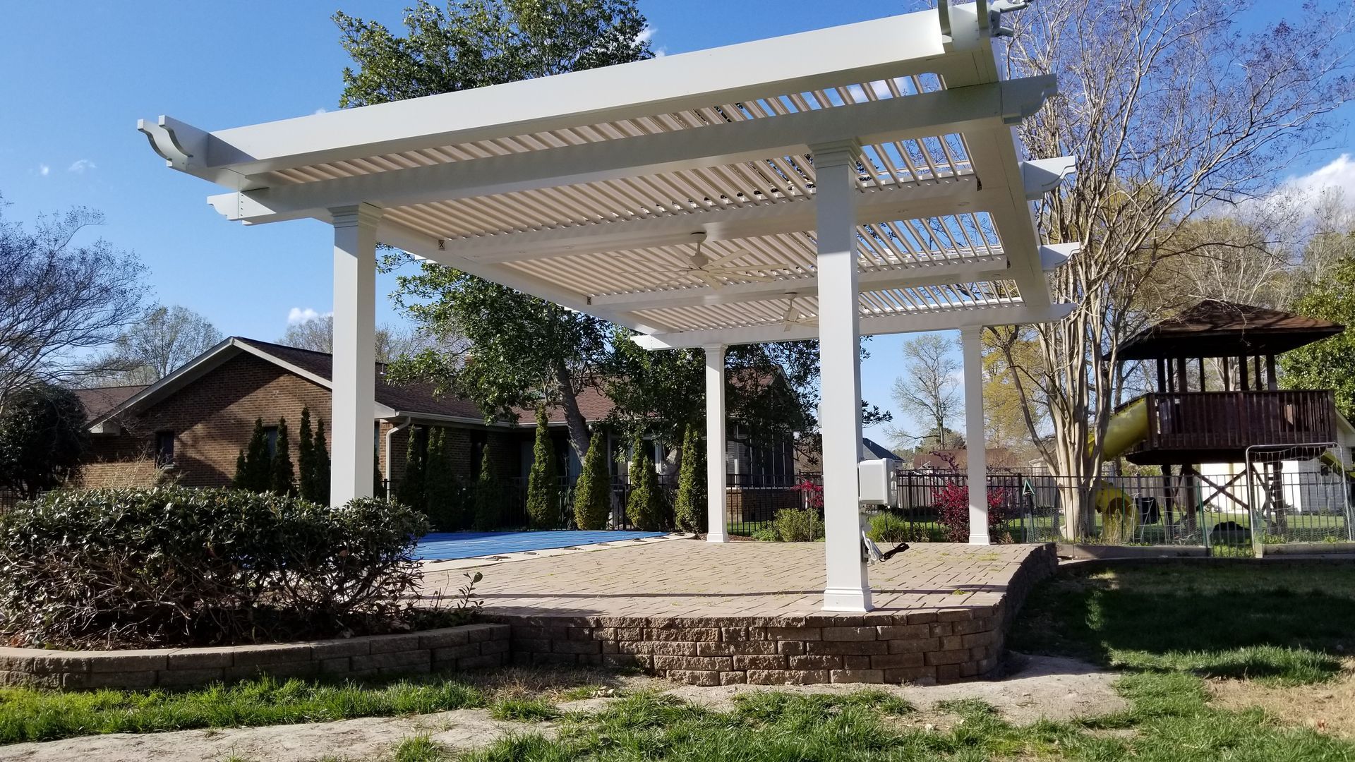 A white pergola is sitting next to a pool in a backyard.