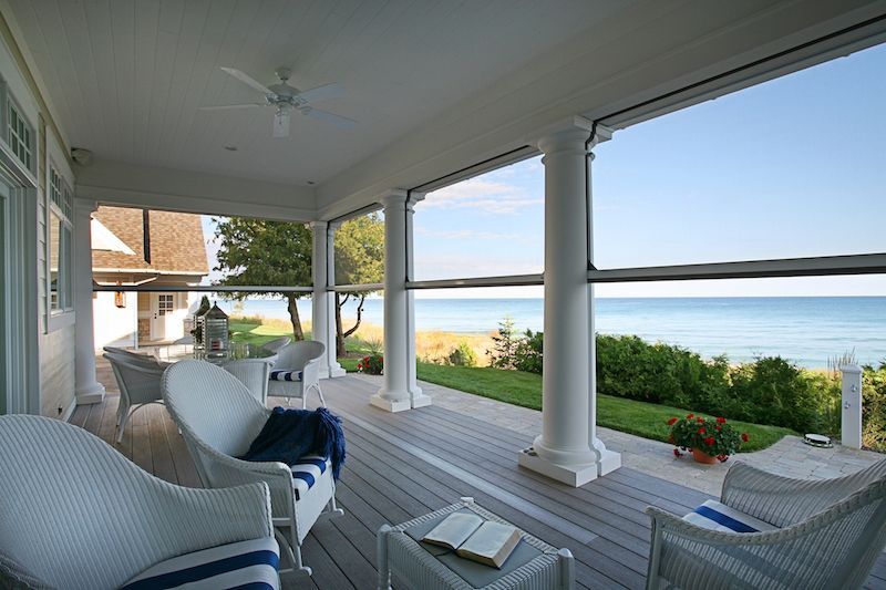 A porch with chairs and a table with a book on it overlooking the ocean.