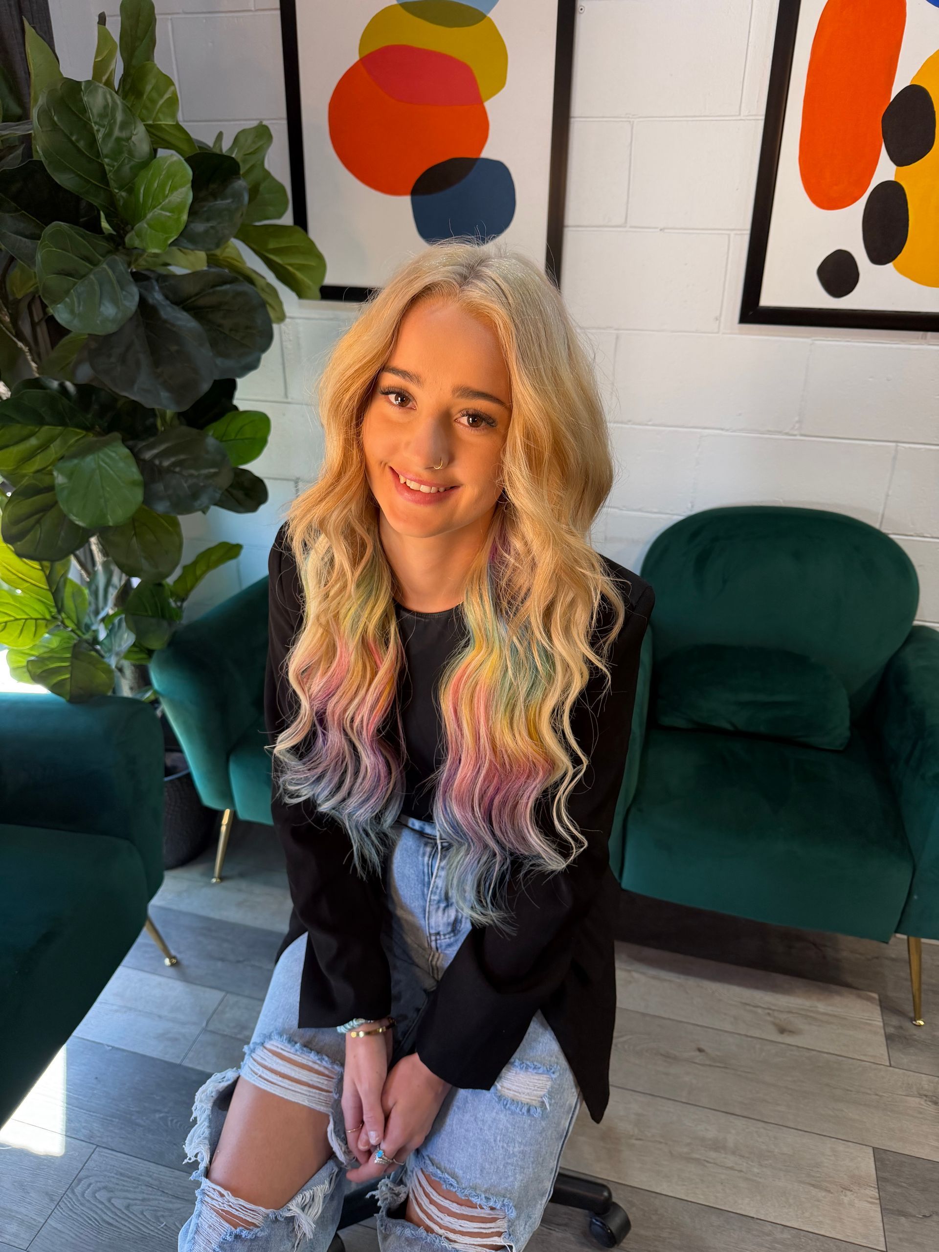 Smiling woman with blonde hair seated on a green couch in a bright living room with colorful wall art.