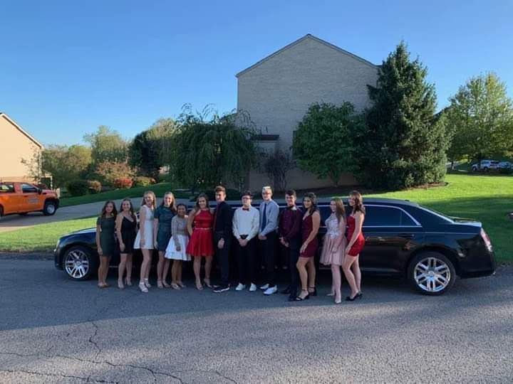 A group of people are posing for a picture in front of a limousine.