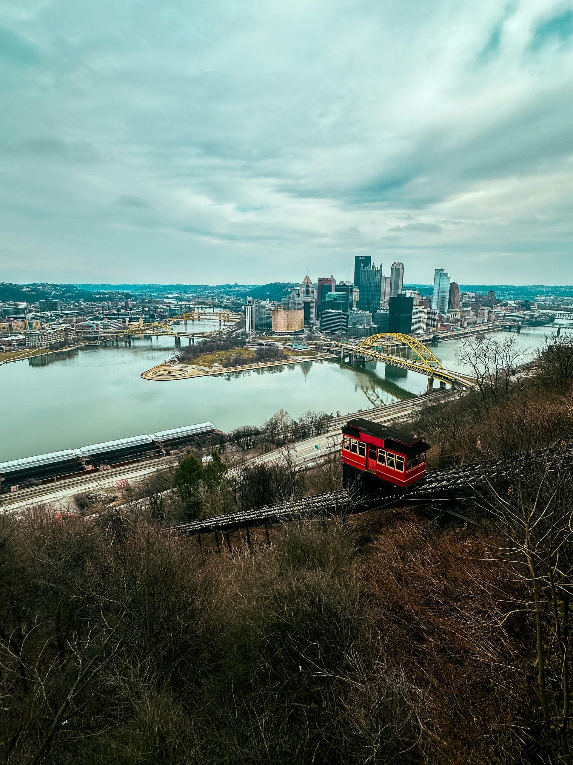 A red train is going down a hill overlooking a city and a river.