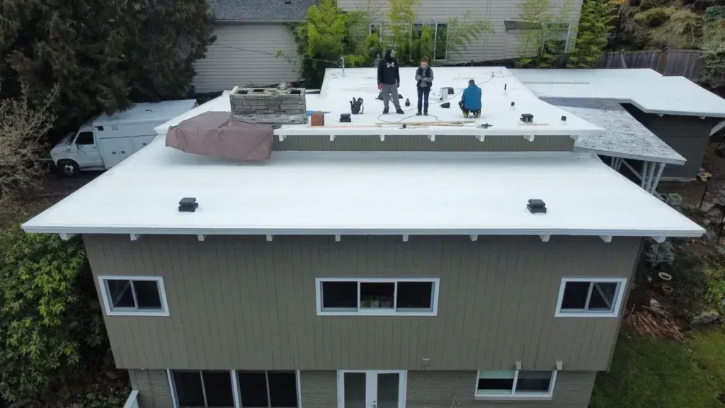 Three people on a white rooftop, inspecting or working. Olive-green house, white trim.