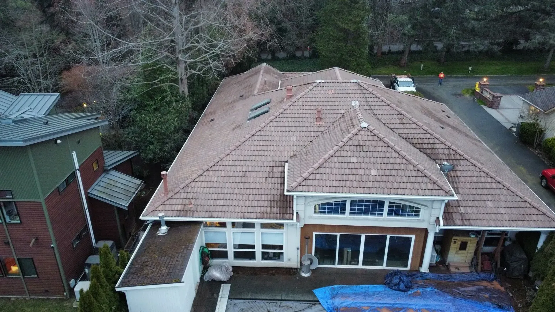 Aerial view of a house with brown tile roof and a modern brick building to the left.