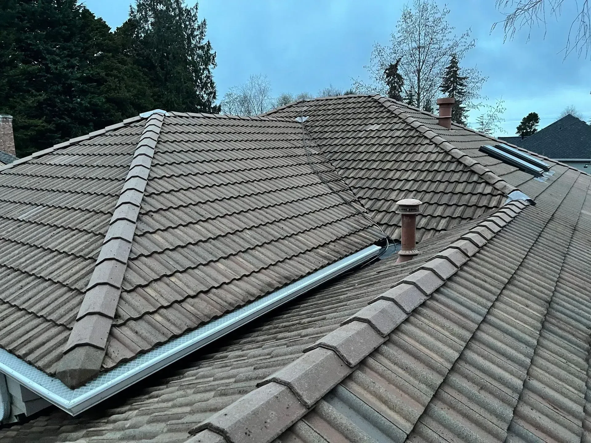 Brown tile roof with gutters, chimneys, and sky.