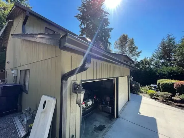 A house with open garage door, car inside, black gutters, sunny day.