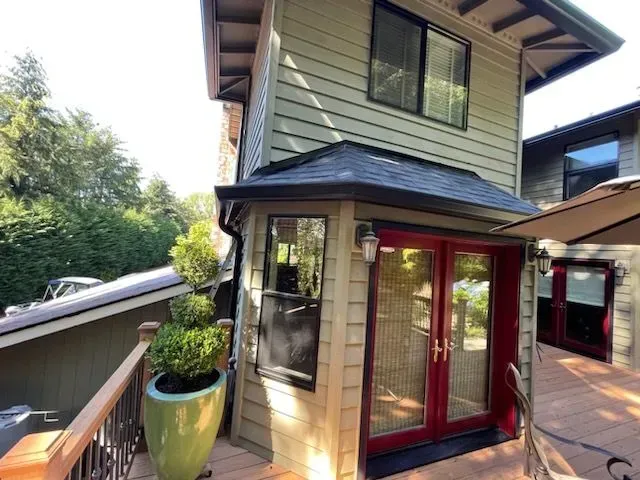 A two-story house with red doors and a green accent. A deck and potted topiary are visible.