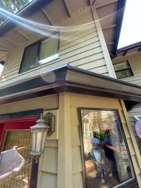 Exterior corner of a house with tan siding, windows, brown trim, and a hanging light fixture.