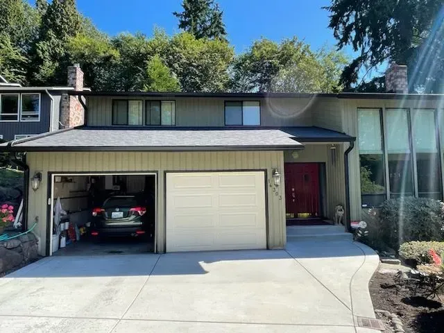 Two-story house with attached garage and red front door; driveway; trees in background.