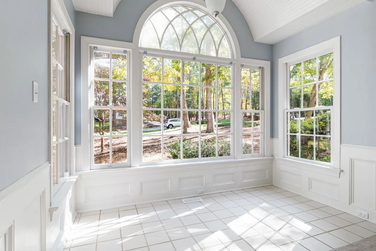 Sunroom with white windows and molding, blue walls, and sunlight on the white tiled floor.