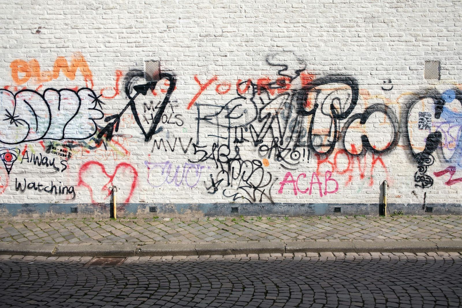 Brick wall covered in graffiti: hearts, text, and tags in various colors. Pavement in front.